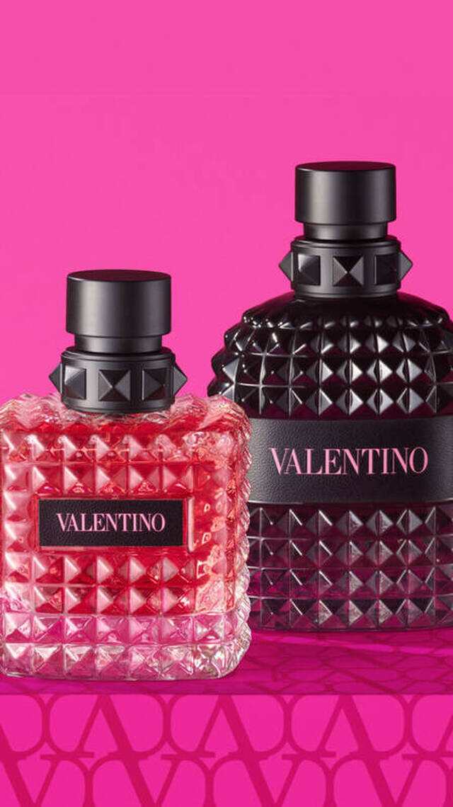 Deux flacons de parfum Valentino sur un fond rose vif, l'un rose et l'autre noir, avec un emballage orne de motifs.
