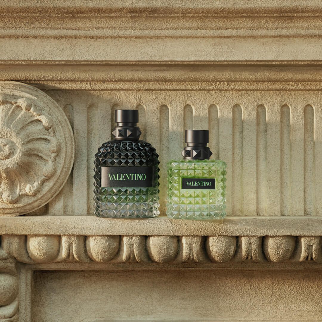 Un mannequin presente un flacon de parfum Valentino, vetu d'une chemise verte vif, dans un cadre naturel elegant.