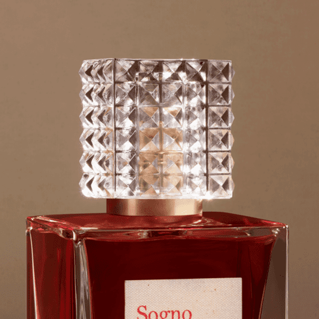 Bouteille de parfum elegante avec un capuchon en cristal, sur fond beige.
