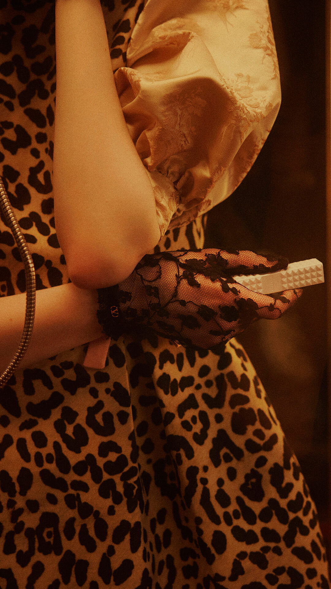 Une femme portant des gants en dentelle noire, tenant le SPIKE VALENTINO IVORY, appuie sur le clavier d un telephone vintage.