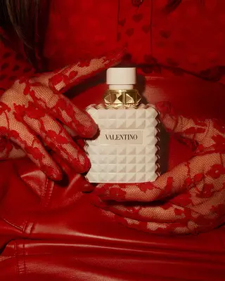 Une femme en rouge, portant des gants en dentelle rouge delicatement ornes, tient BORN IN ROMA IVORY DONNA.