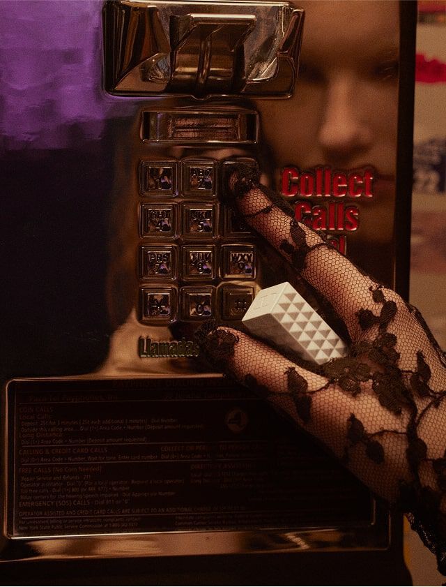 Une femme portant des gants en dentelle noire, tenant le SPIKE VALENTINO IVORY, appuie sur le clavier d un telephone vintage.