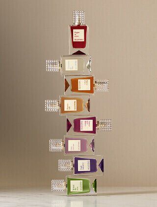 Une rangee de huit flacons de parfum Valentino de couleurs variees, chacun avec un bouchon transparent texture, alignes sur une surface claire devant un fond beige