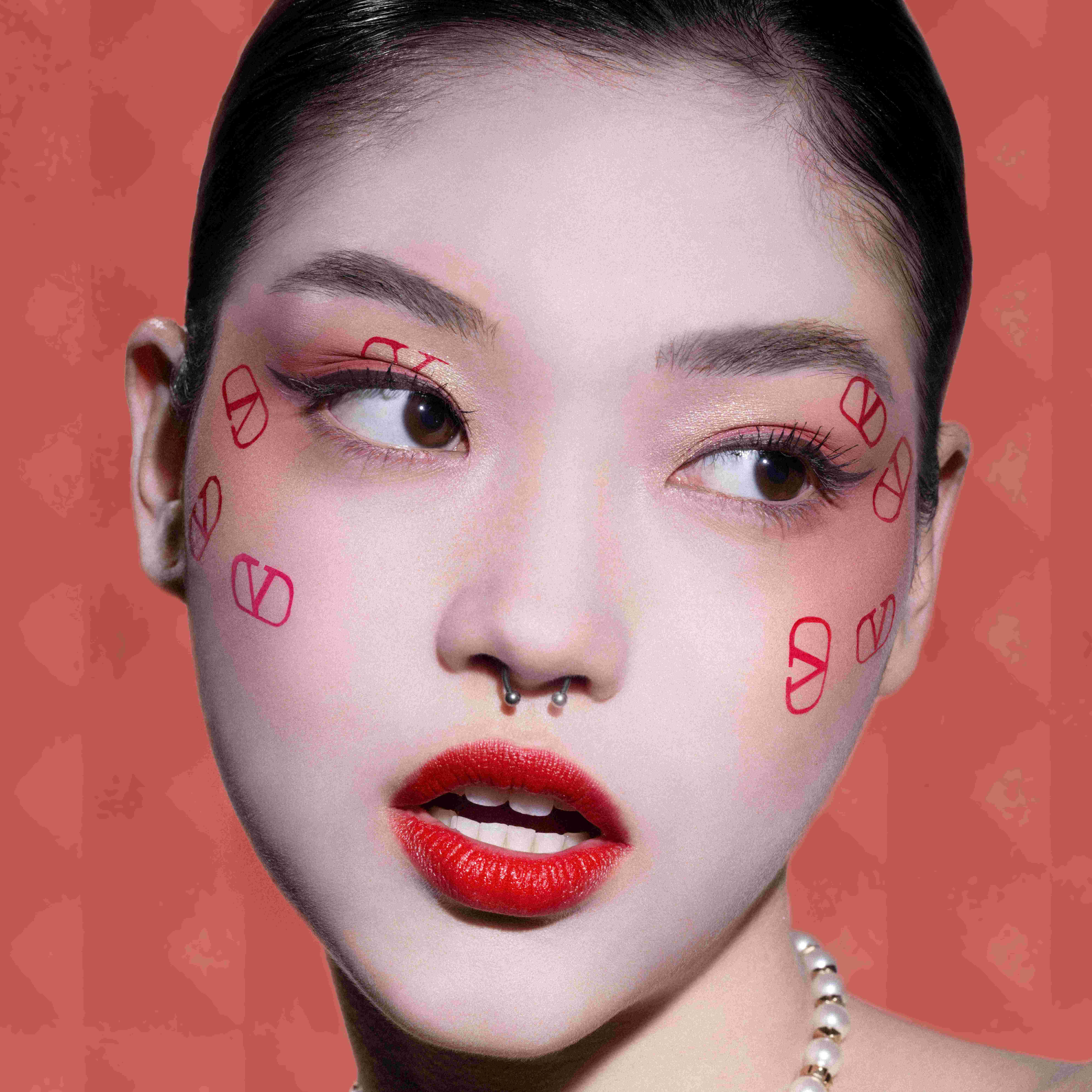 Femme avec un maquillage artistique, traits rouges sur le visage, fond rose texture.