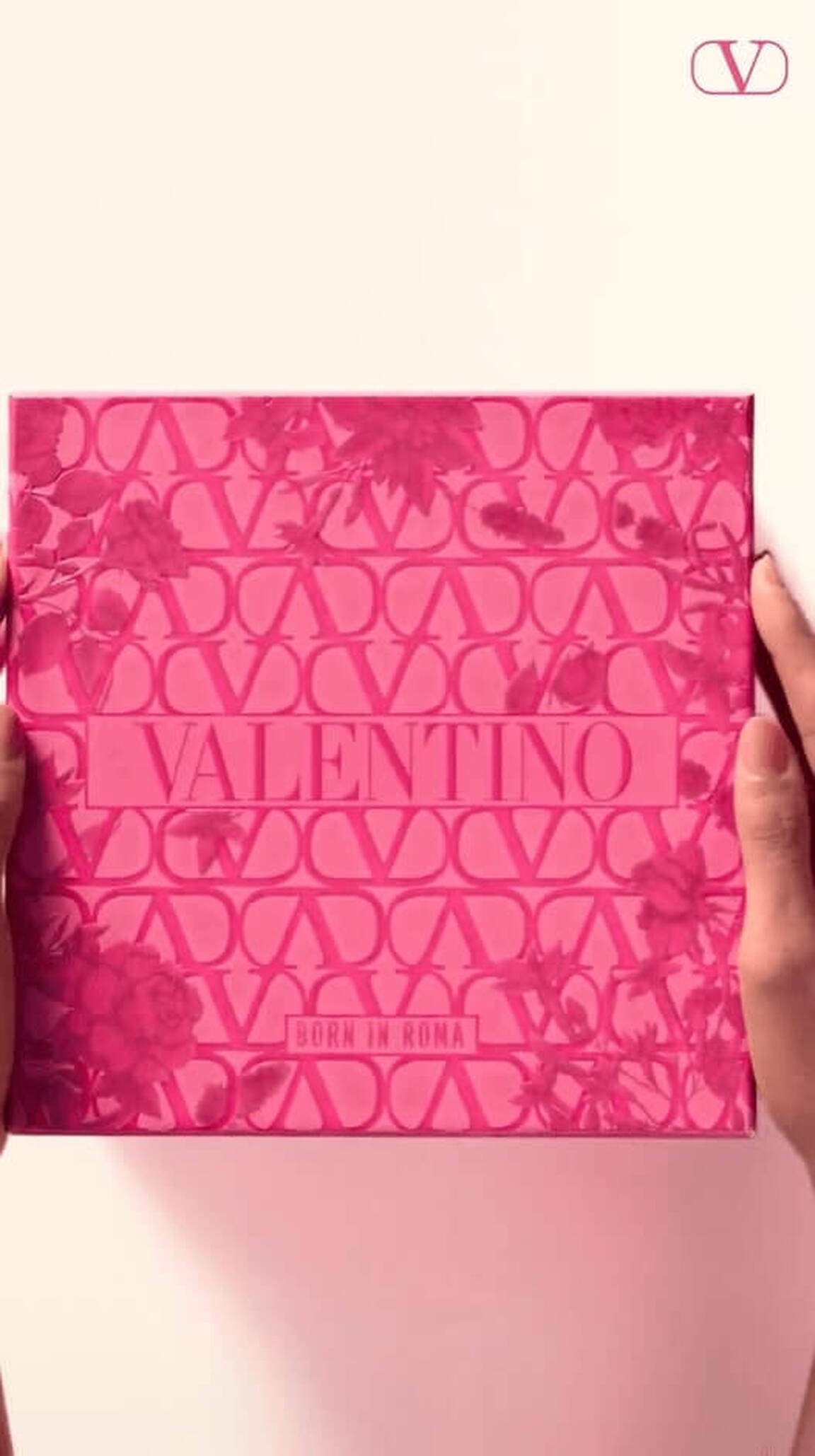 A person holds a pink Valentino box adorned with floral patterns, featuring the text 'VALENTINO' and 'BORN IN ROMA.'
